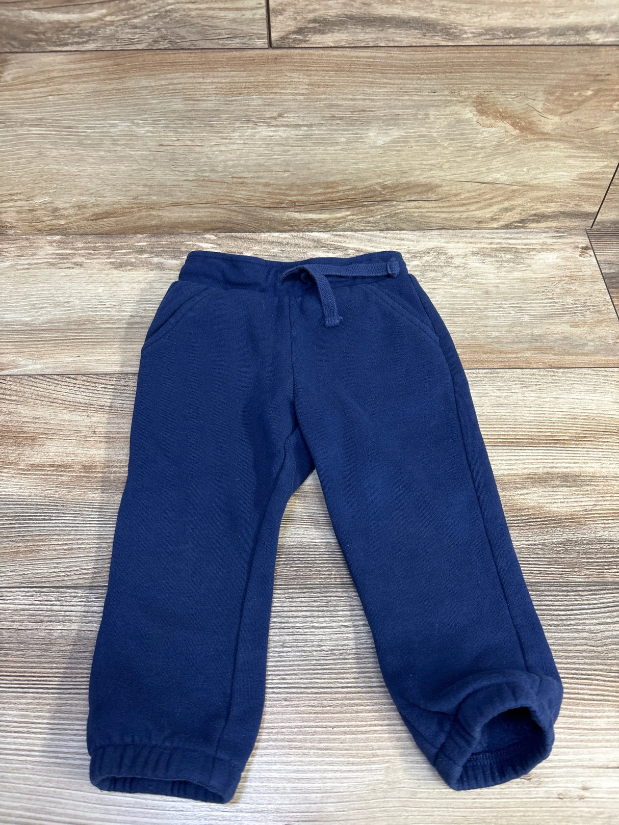 Top down view of Okie Dokie navy drawstring joggers with drawstring waistband, pockets and elastic cuffs on wood background