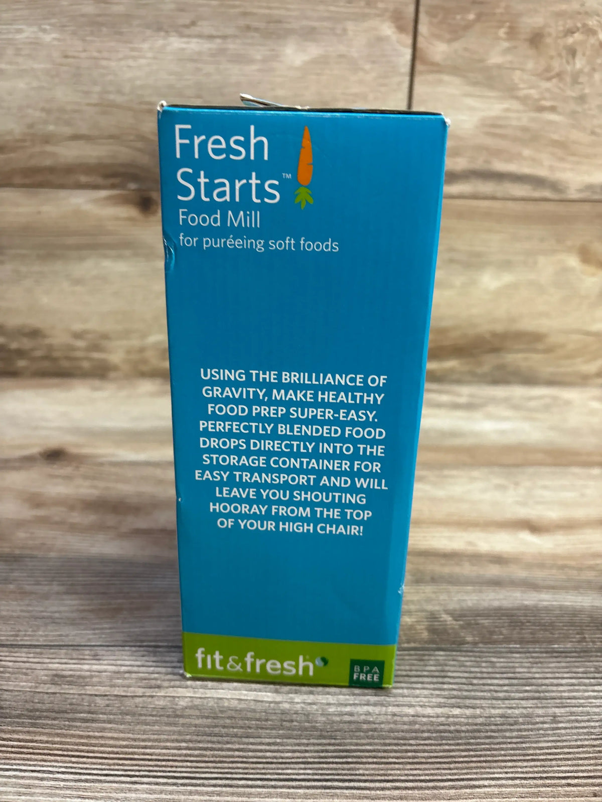 Front view of Fit & Fresh Fresh Starts green food mill box showcasing soft-food puréeing with wood-grain background
