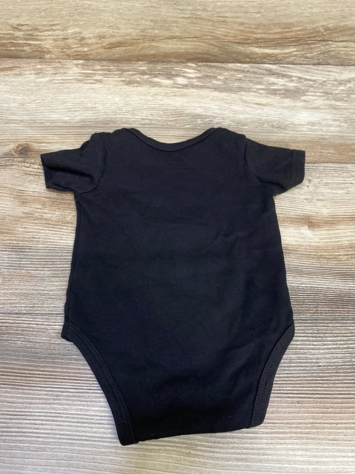 Black short-sleeve baby onesie laid flat on wood grain surface