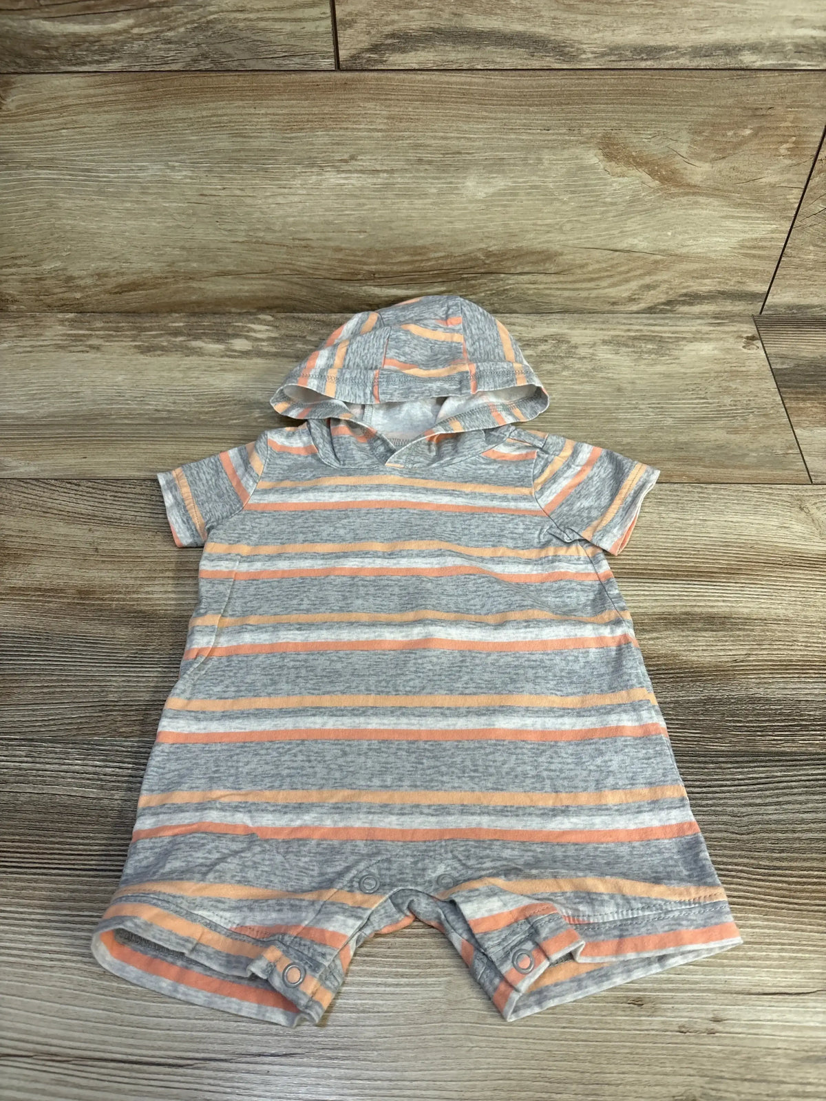 Front view of grey hooded shortie romper with peach and white stripes, short sleeves and crotch snap closures on wood background