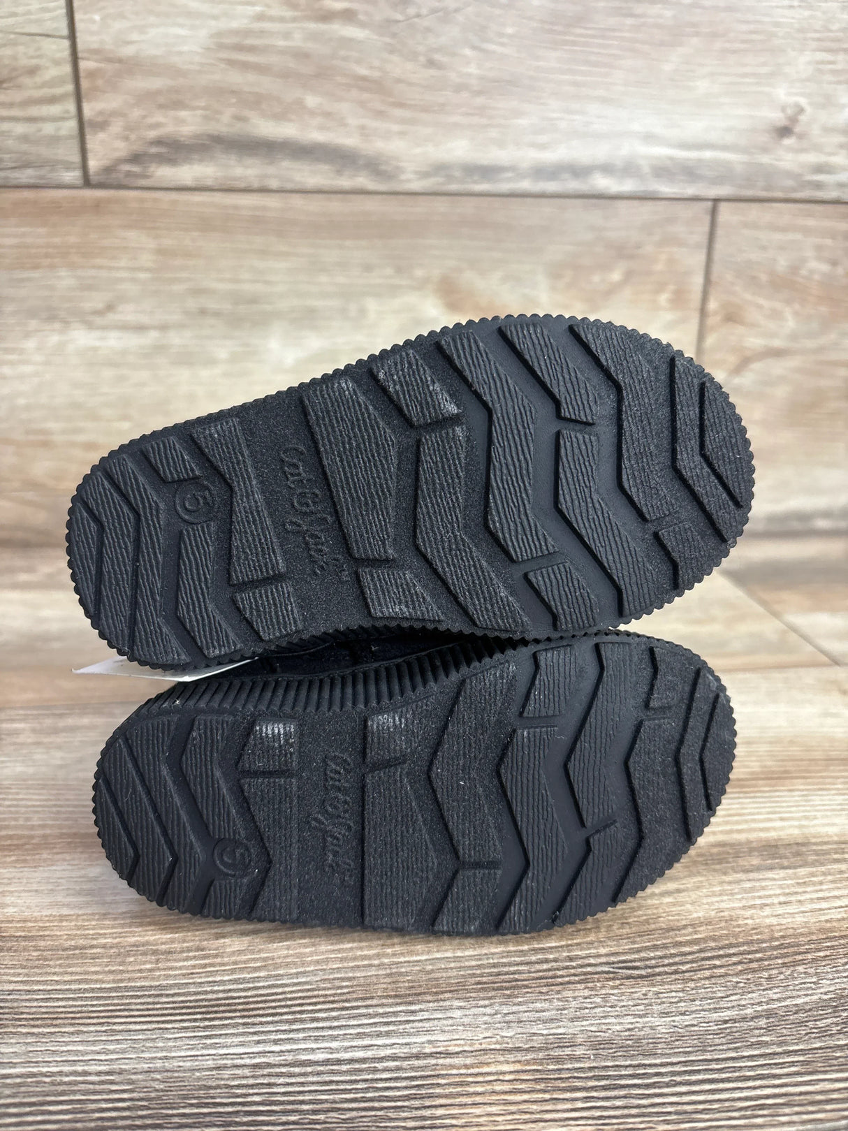 Close-up of black toddler shoe soles with textured non-slip pattern on wood floor
