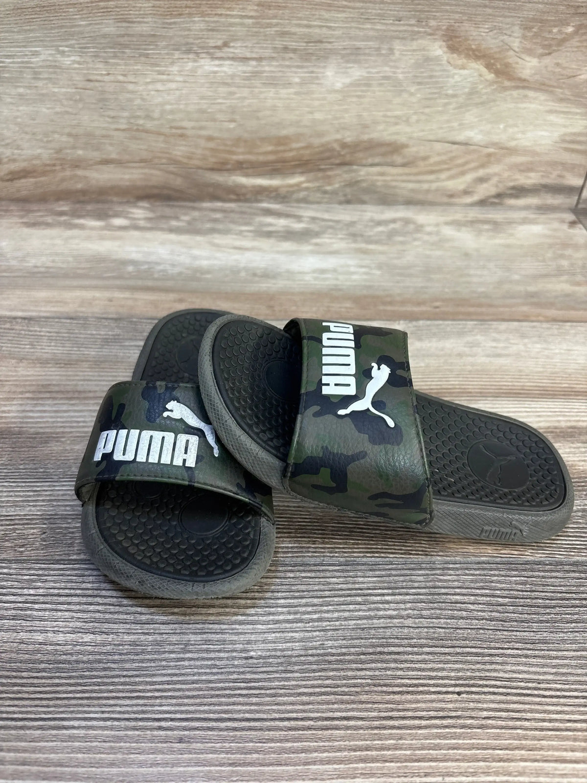 Kids camo Puma slide sandals with logo on wooden background, gently used condition