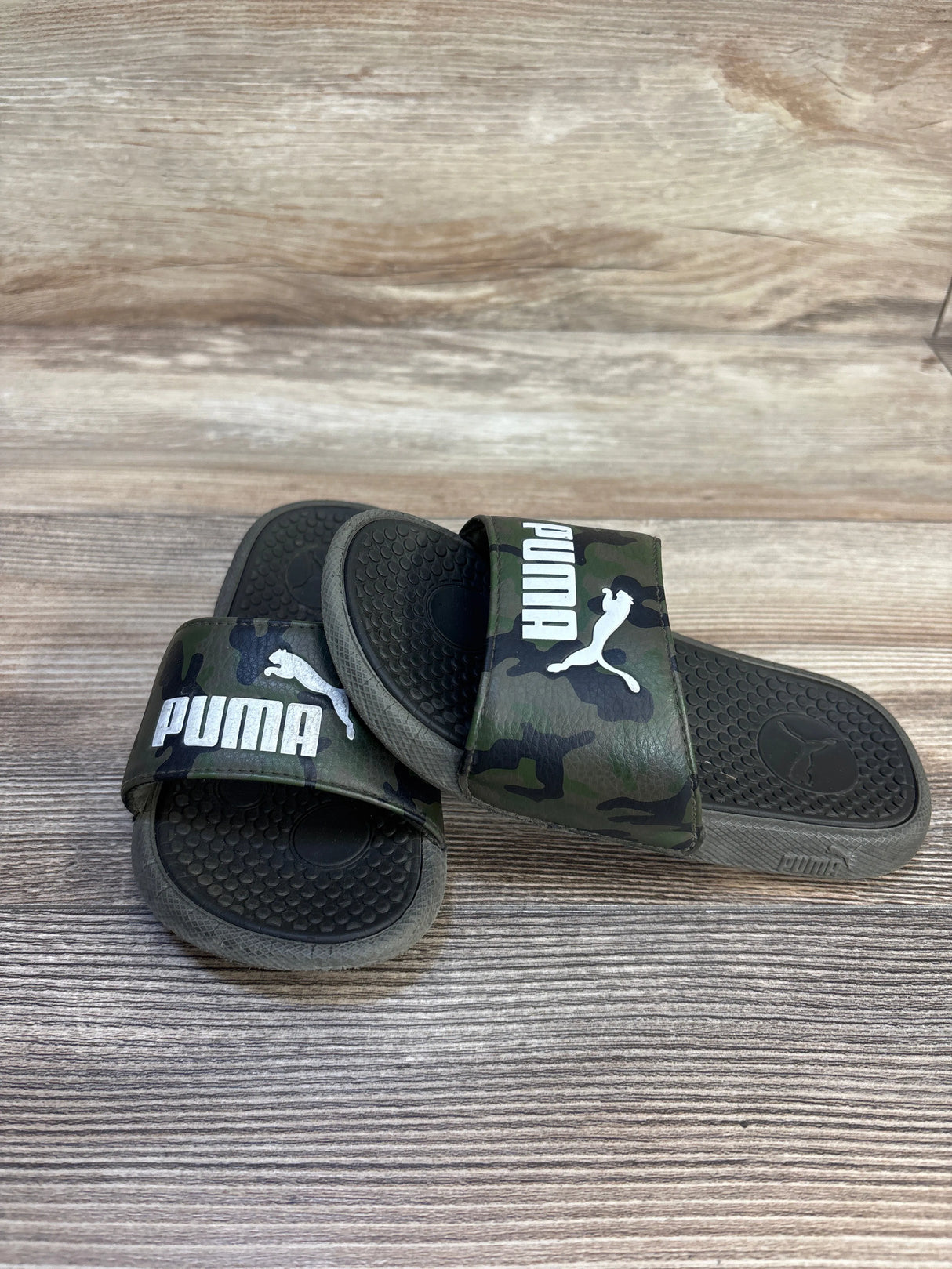 Kids camo Puma slide sandals with logo on wooden background, gently used condition