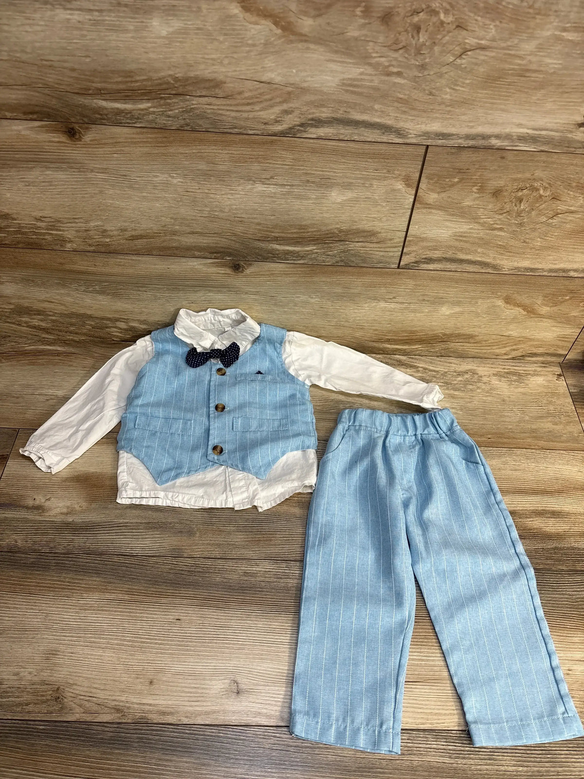 Baby boy formal outfit with light blue pinstripe vest, pants, white shirt, and bow tie on wood floor
