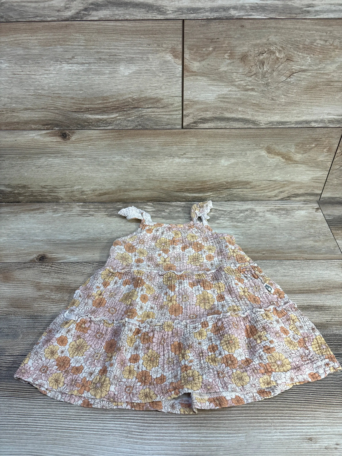 Front view of Rabbit + Bear organic floral tiered dress in beige showcasing sleeveless tiered design on a wood-grain background