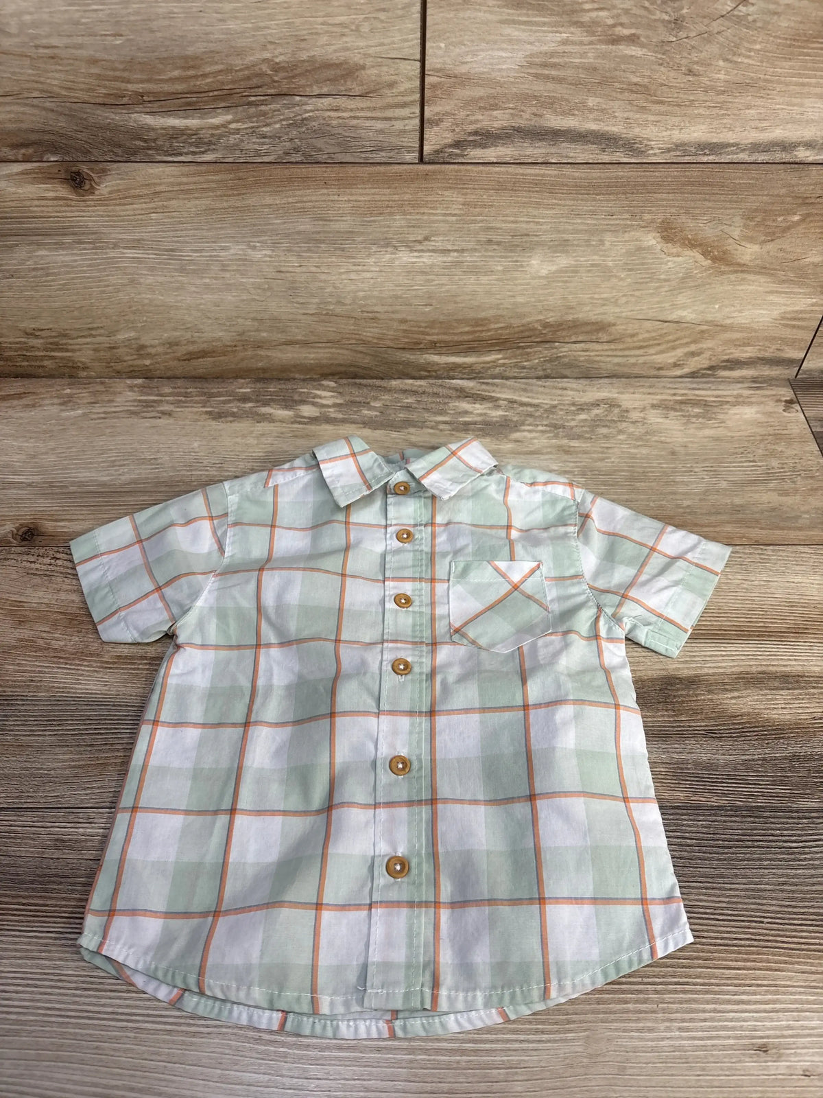 Front view of toddler green and white plaid button-up shirt size 4T showcasing short sleeves, chest pocket and wooden-look buttons on wood background
