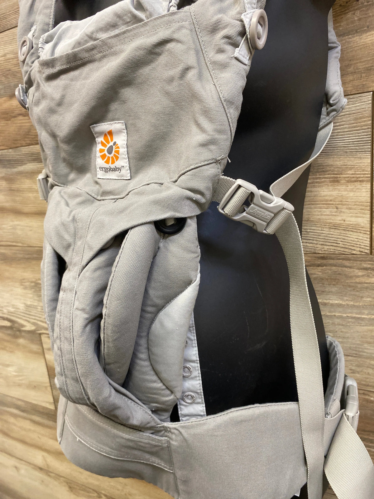 Close up view of Ergobaby Omni 360 carrier in Pearl Grey showing logo, padded straps and waist belt on black mannequin