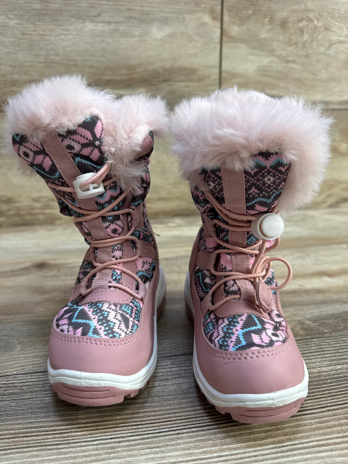 Front view of Nova Mountain toddler snow boots showcasing pink faux-fur cuffs, patterned fabric uppers, and toggle laces on wood floor