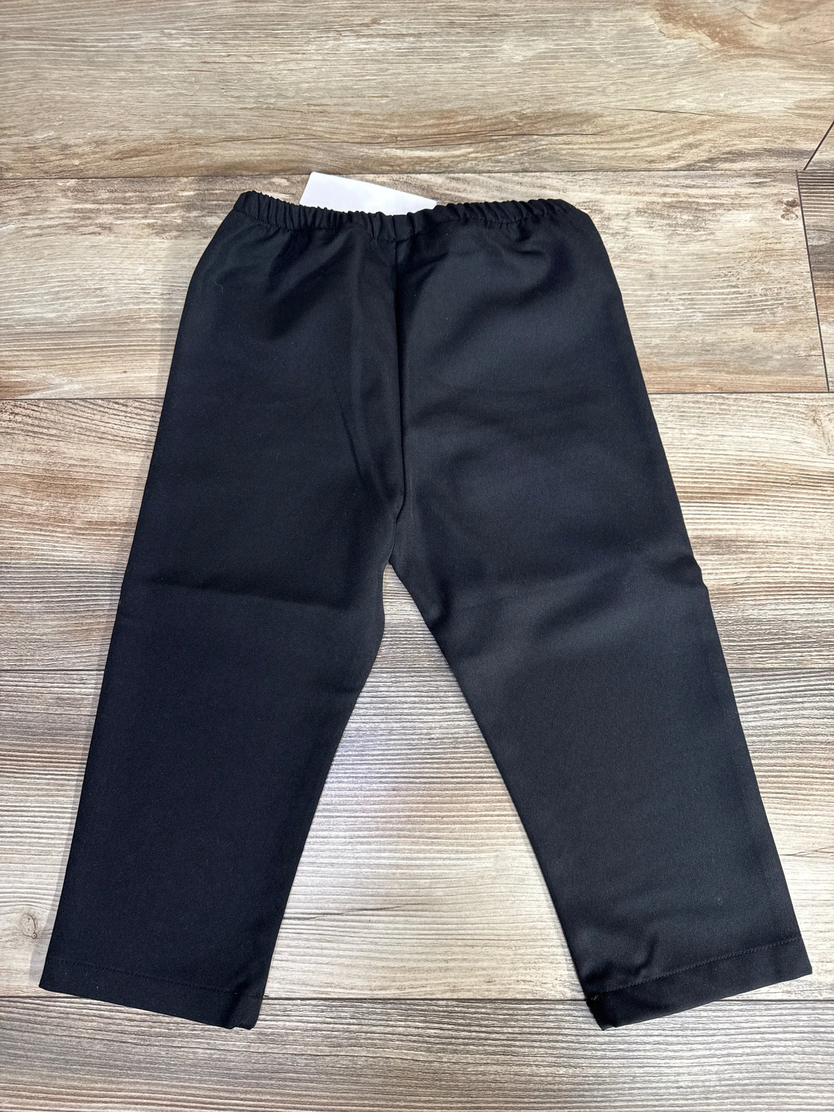 Black elastic waist toddler pants laid flat on wooden floor, children's clothing resale item