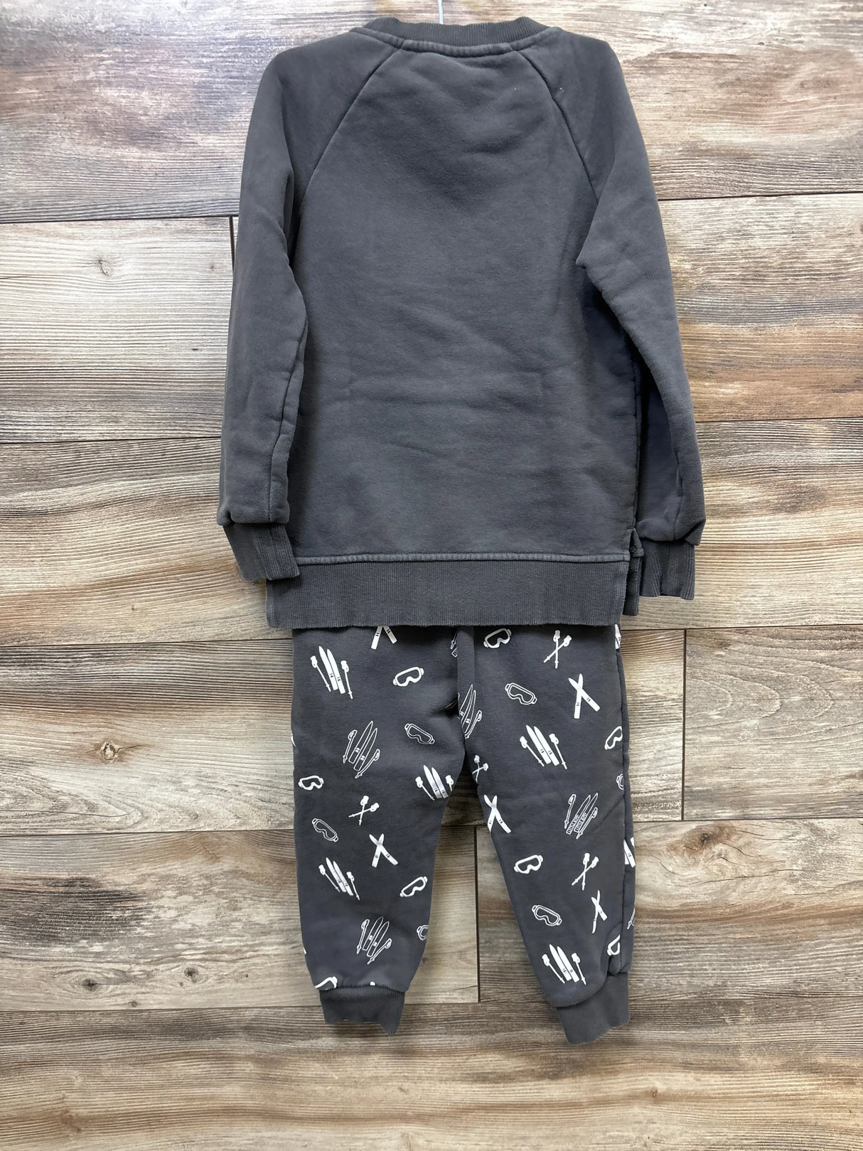 Back view of kids' dark gray sweatshirt and ski-themed print pants on wooden floor