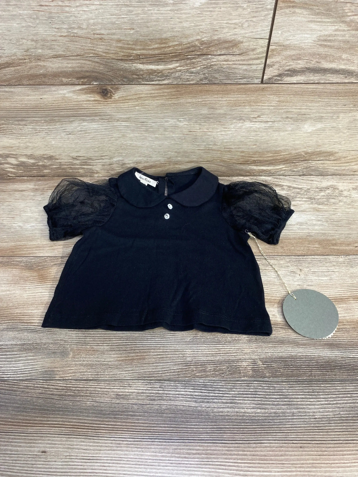 Flat lay of toddler black tulle puff sleeve top showing Peter Pan collar and two-button front on wood background
