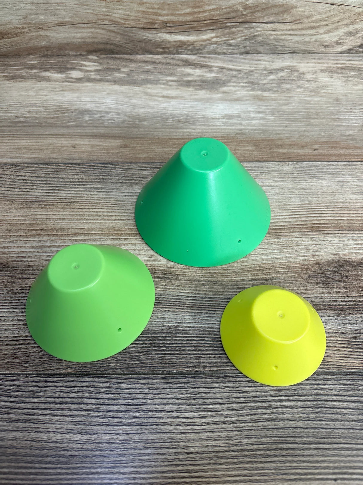 Set of three colorful plastic cones for kids on wood background, green, lime, and yellow.