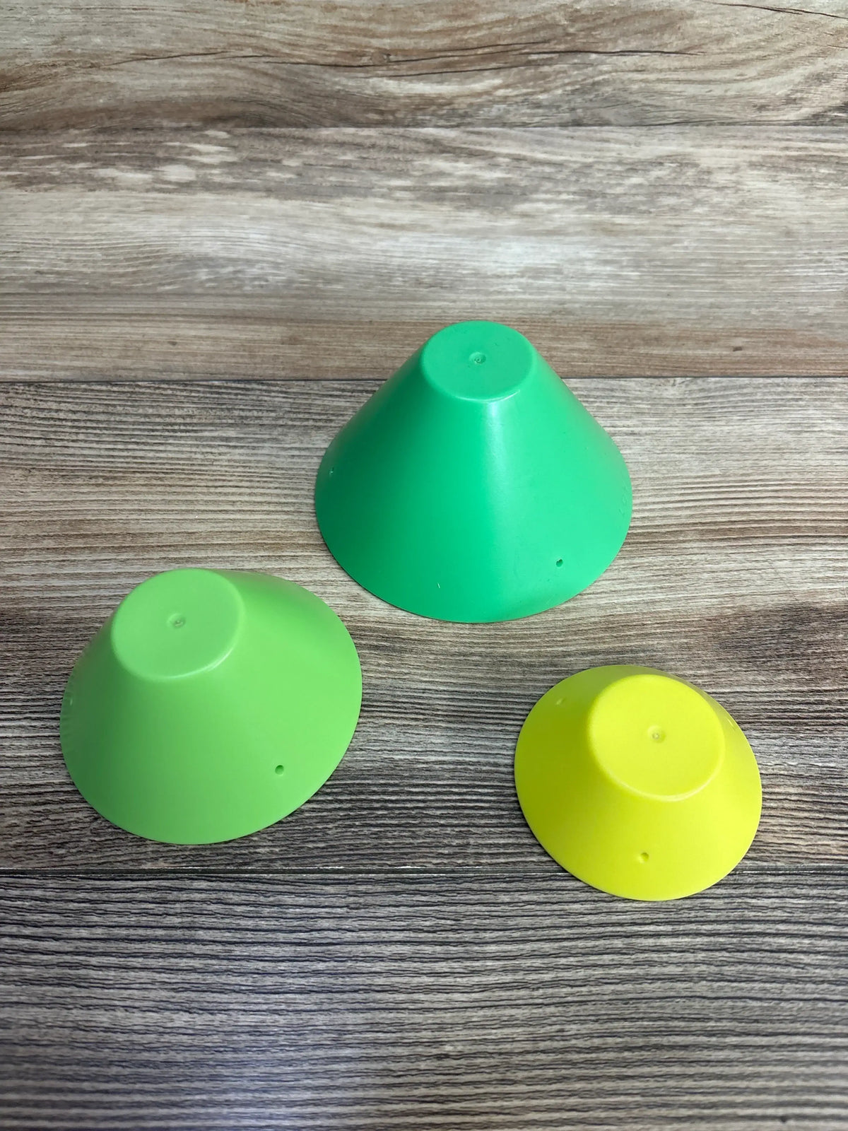 Set of three colorful plastic cones for kids on wood background, green, lime, and yellow.