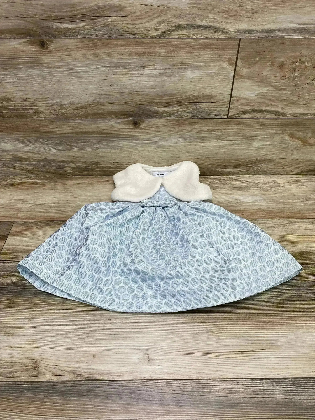 Flat-lay of Popatu blue polka-dot dress with white faux-fur vest showing gathered skirt and textured dots on wood floor background