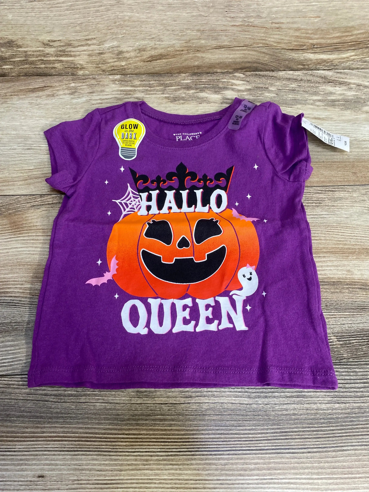 Flat lay of purple toddler shirt (12-18M) with orange pumpkin and Hallo Queen graphic and glow sticker on wood