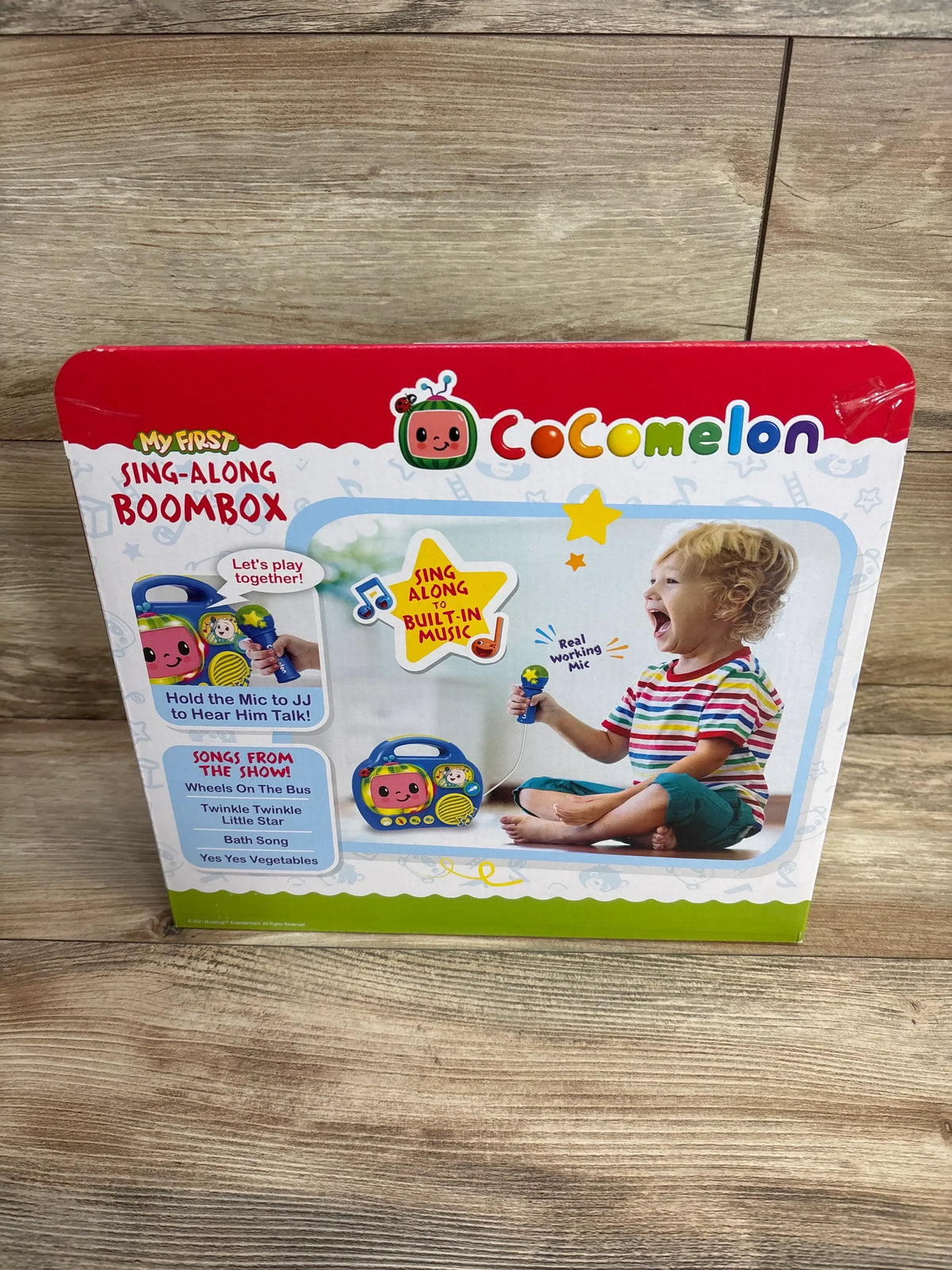 Cocomelon sing-along boombox toy in box, child playing with microphone, wooden floor background