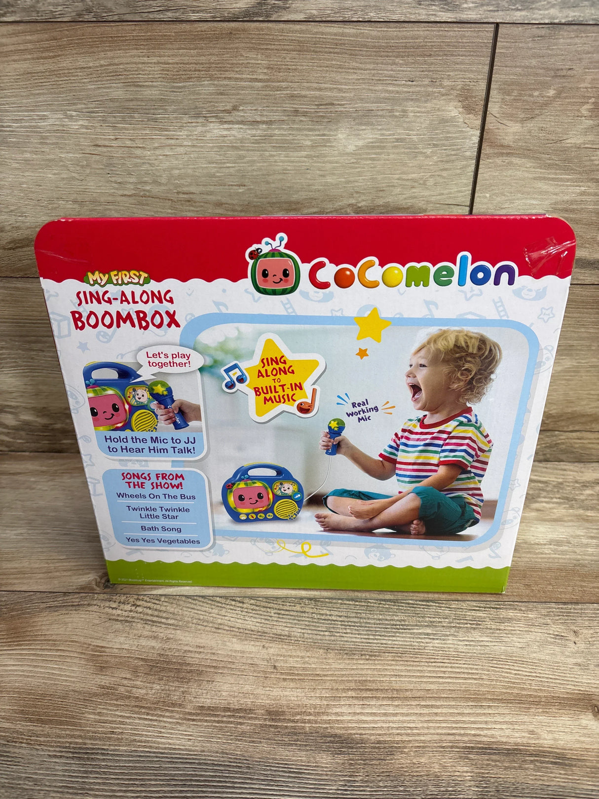 Cocomelon sing-along boombox toy in box, child playing with microphone, wooden floor background