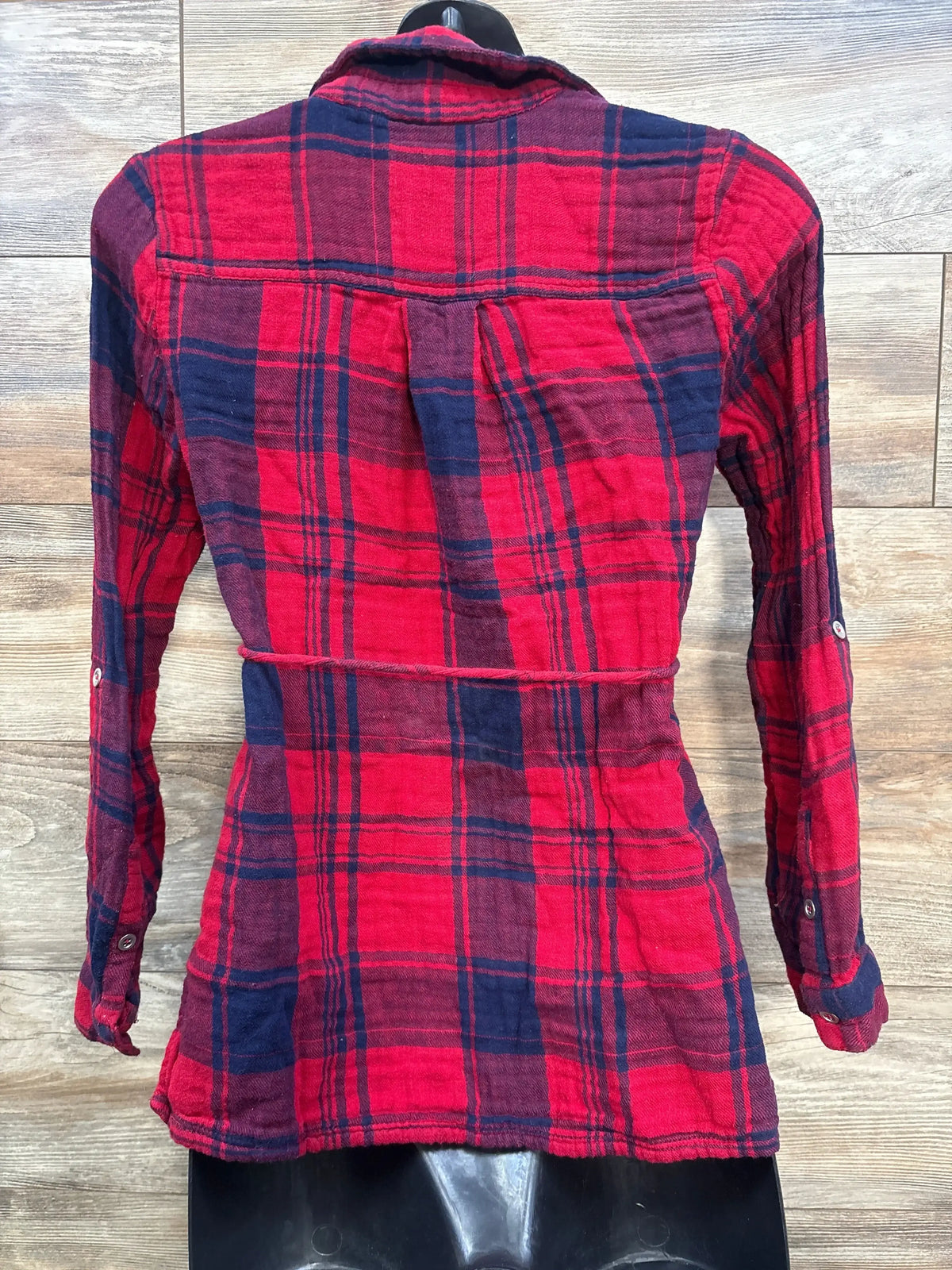 Back view of red and navy maternity plaid long-sleeve button-up shirt showcasing back pleat and waist seam on wood background