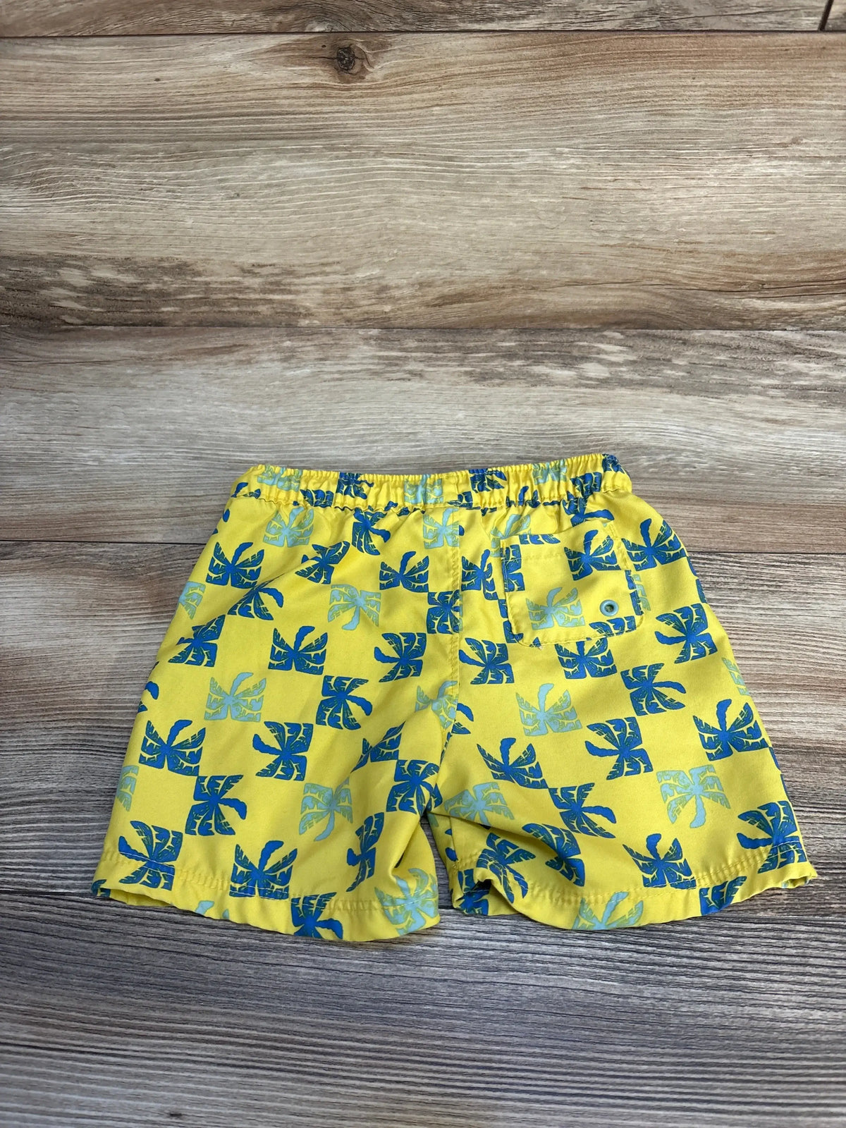 Yellow kids shorts with blue palm leaf print, elastic waistband, on wood background