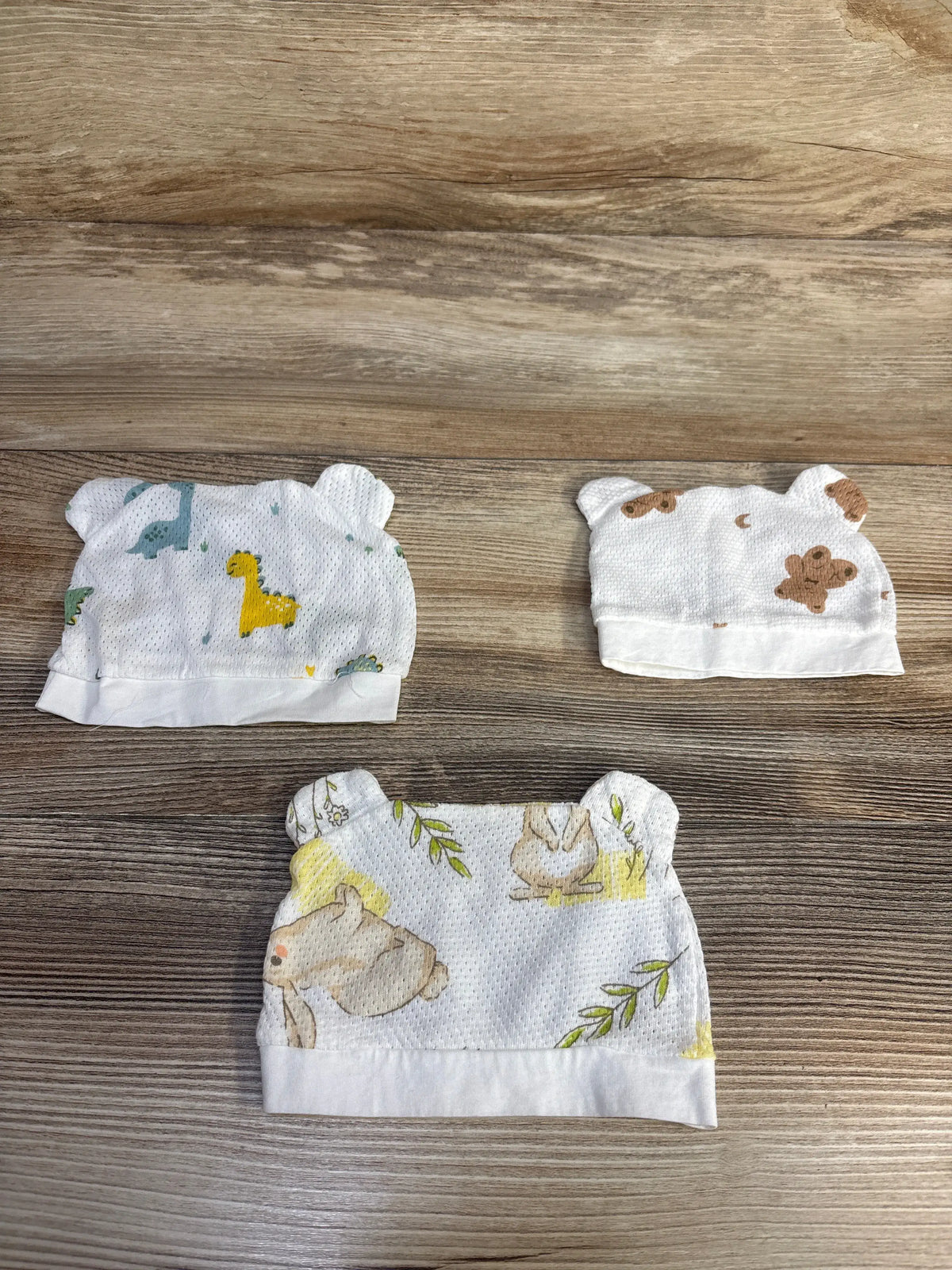 Top view of Mesh Animal Print Newborn Hats with Ears 3pk showing three white mesh hats on a wood grain surface