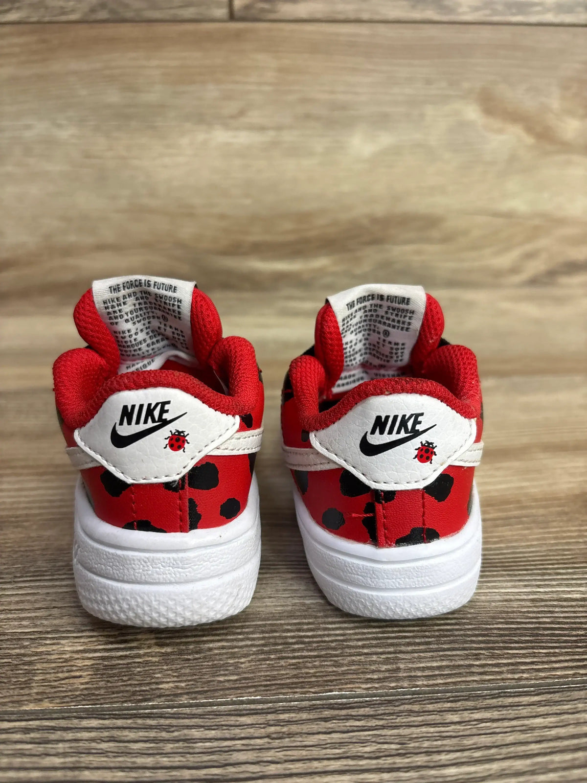 Pair of red and black spotted Nike toddler sneakers with white soles and ladybug logo, wooden floor