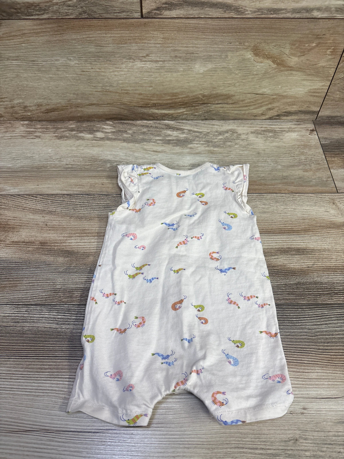Front view of Bout’Chou beige shortie romper, size 6 months, with colorful all-over shrimp print on a wood floor