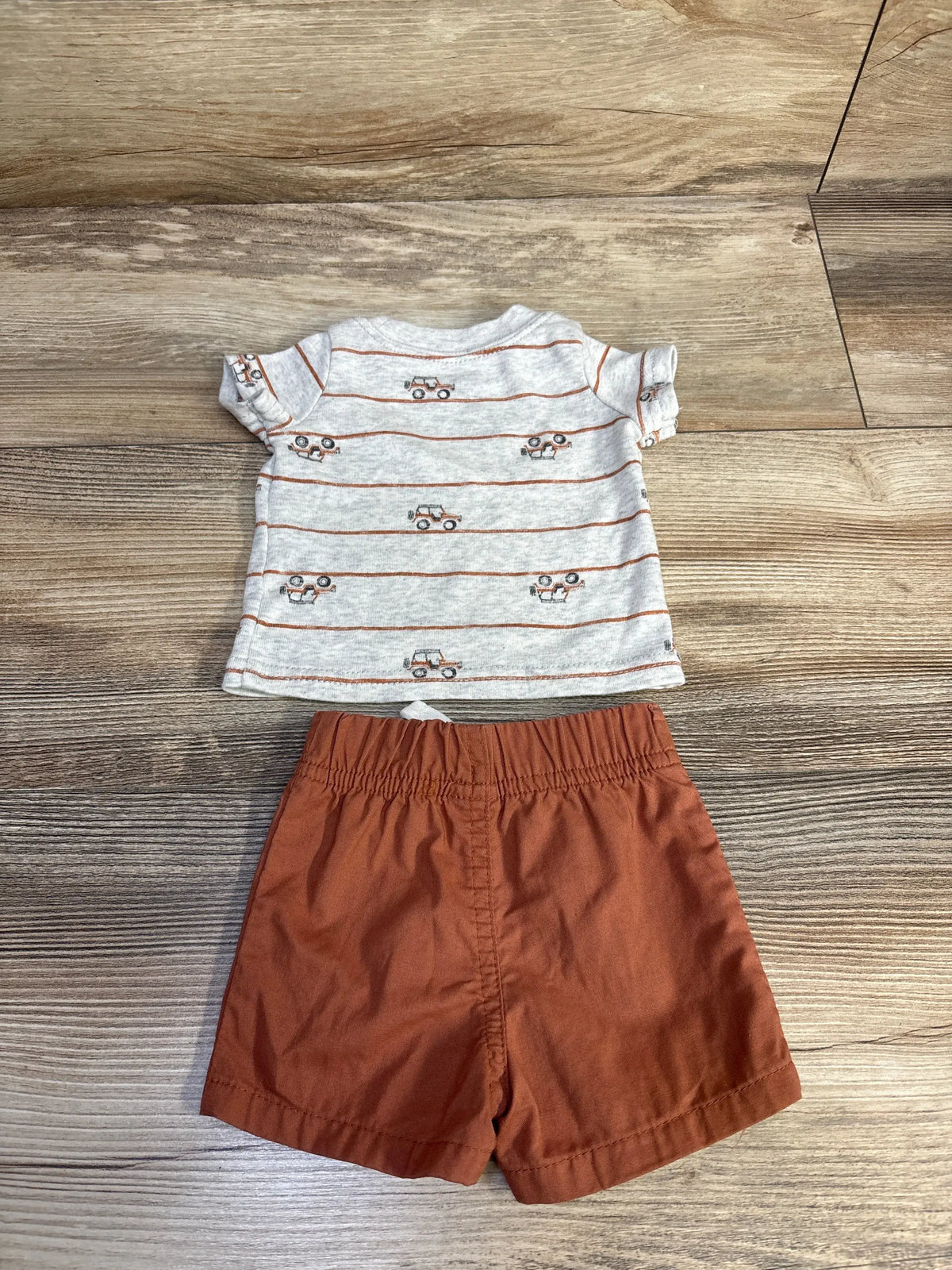 Top view of grey shirt and coordinating shorts showcasing striped shirt with vehicle prints on a wood floor