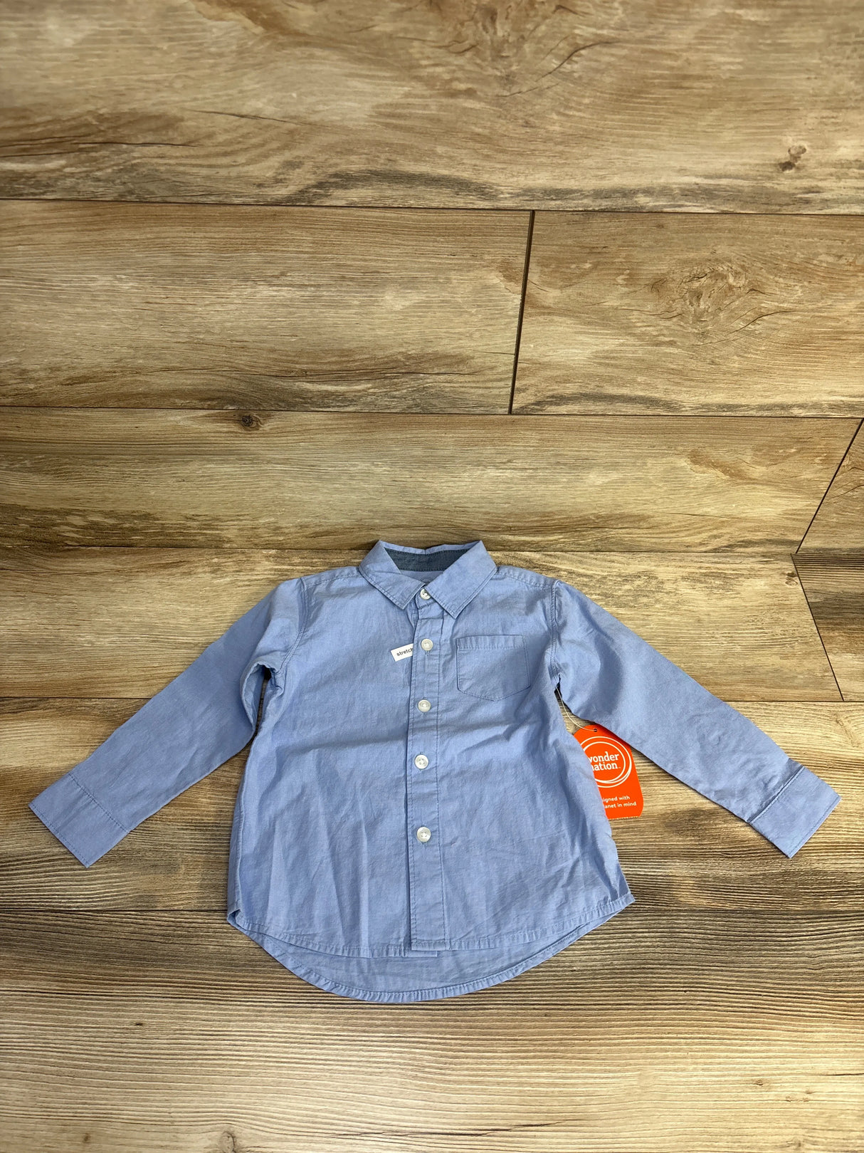 Light blue long-sleeve button-up baby shirt on wooden floor with price tag attached