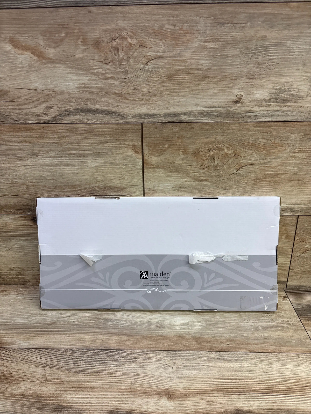 Front view of Malden Baby’s First Year 12-opening picture frame packaging showcasing gray decorative artwork on a wood floor