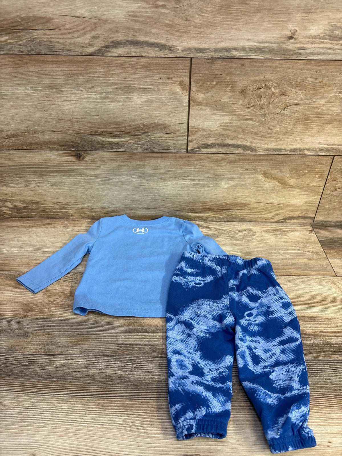 Flat lay of Under Armour 2-piece: light blue long-sleeve shirt with back logo and blue pants with elastic waist on wood