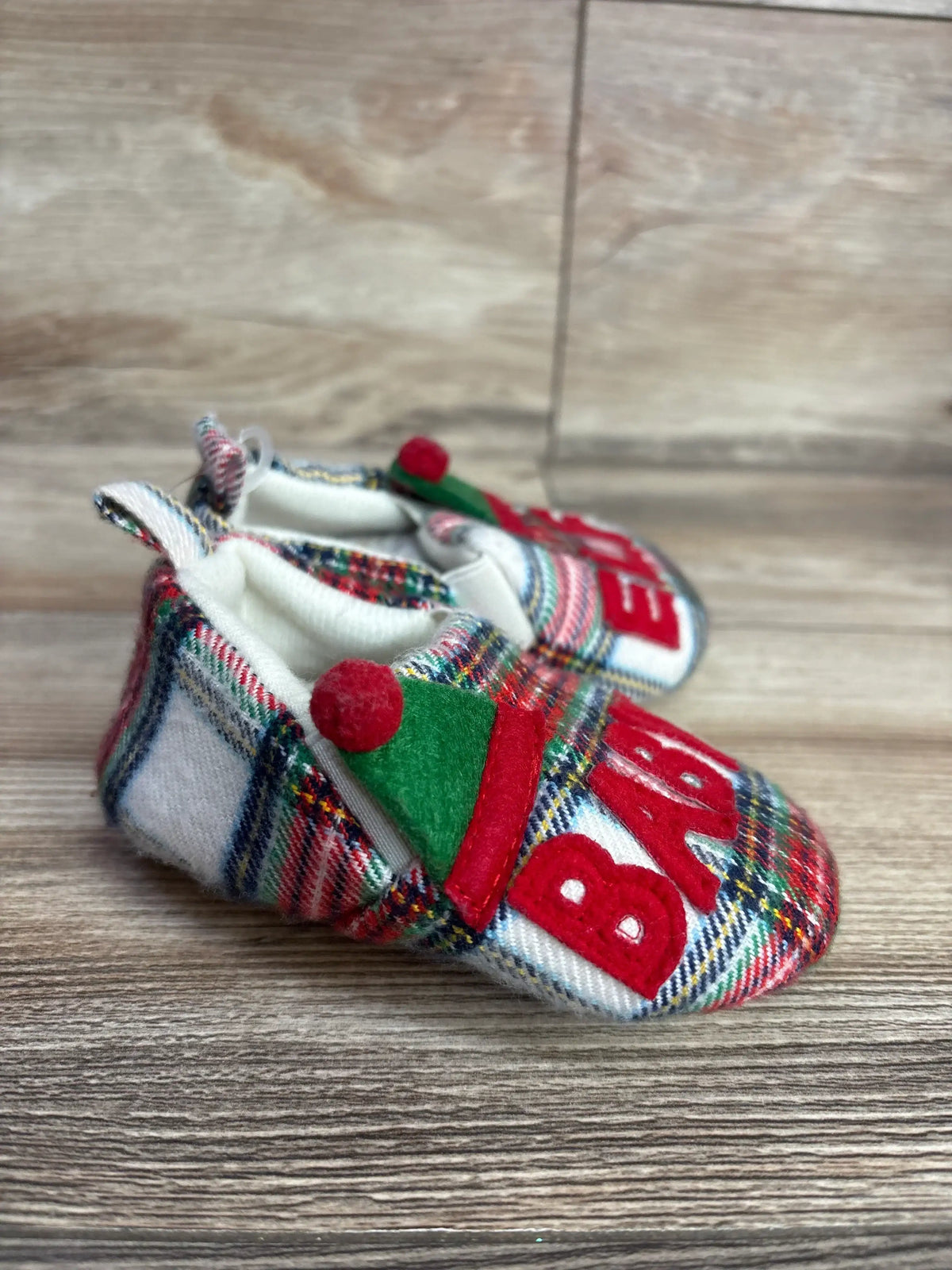 Festive plaid baby booties with red pom-poms and 'BABY' appliqué, perfect for holiday outfits.