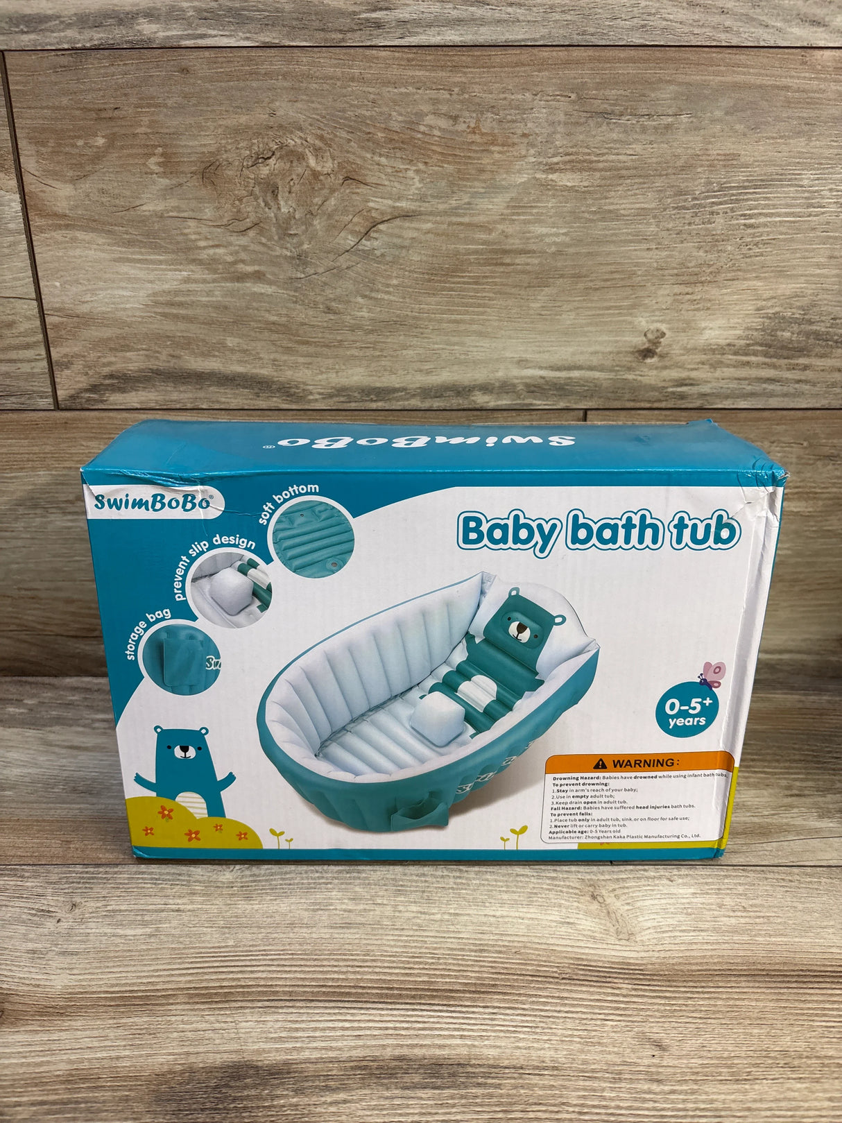 Front of SwimBoBo baby bathtub box showing teal inflatable tub with bear pillow and Baby bath tub text on wood
