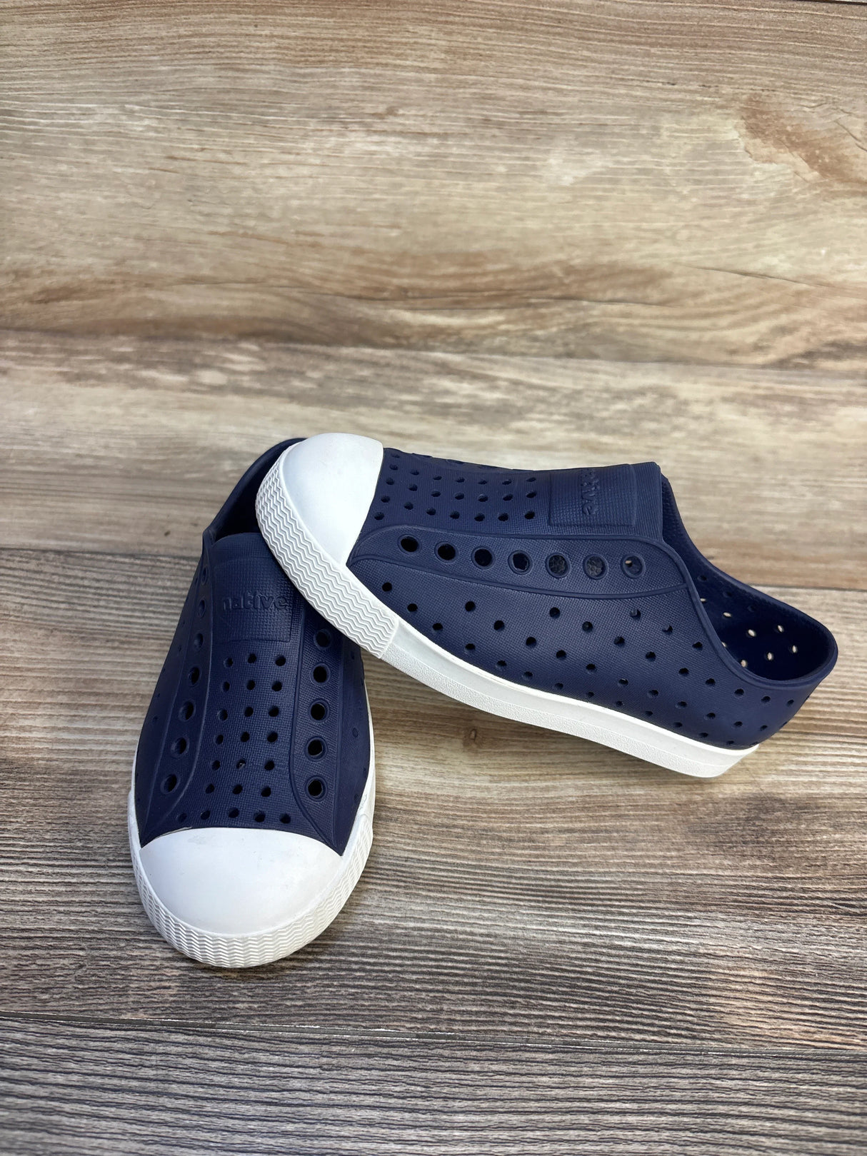 Navy blue slip-on kids shoes with white rubber toe caps and ventilation holes on wood floor