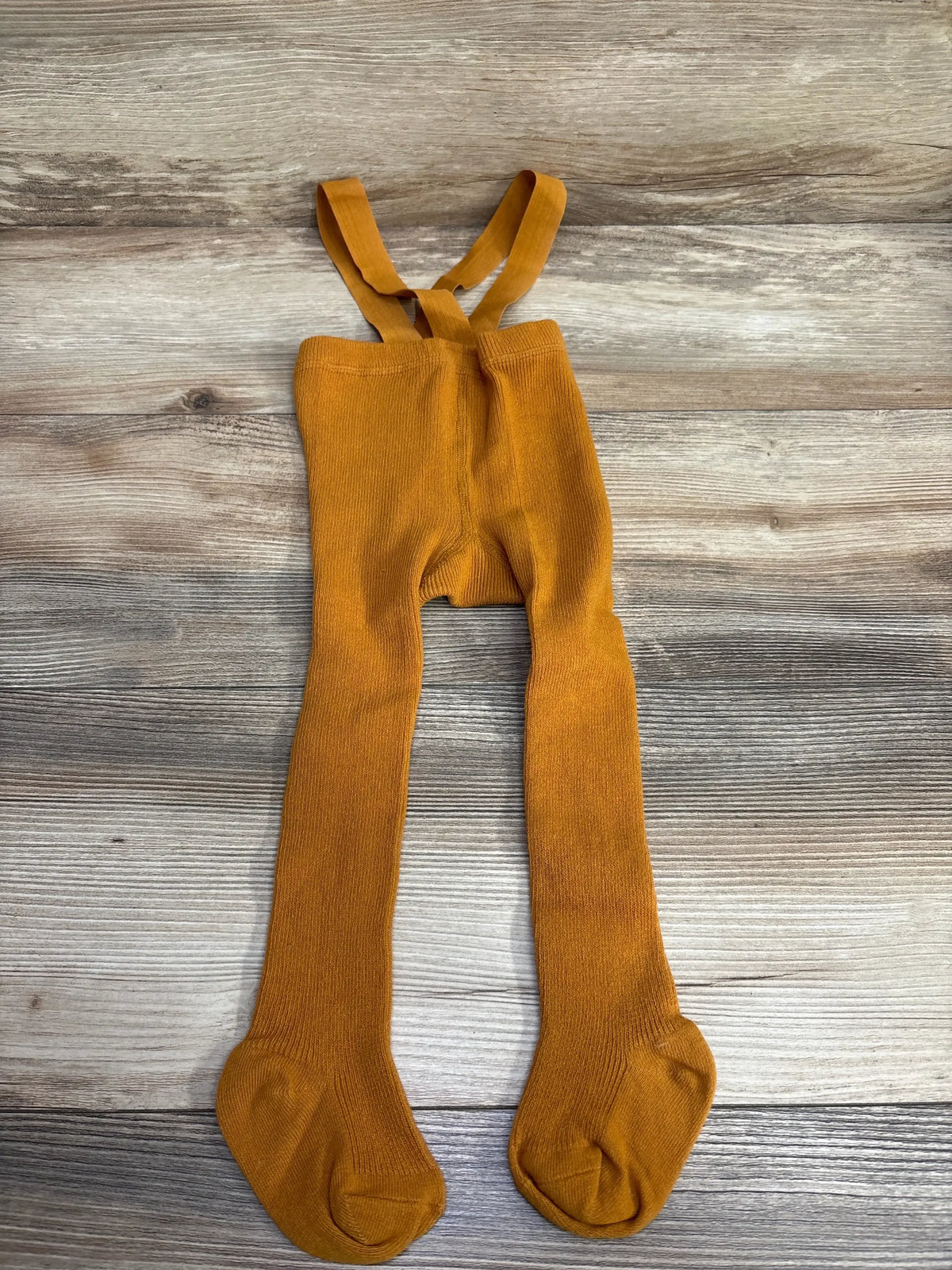Rust orange toddler knit tights with suspenders on wood background