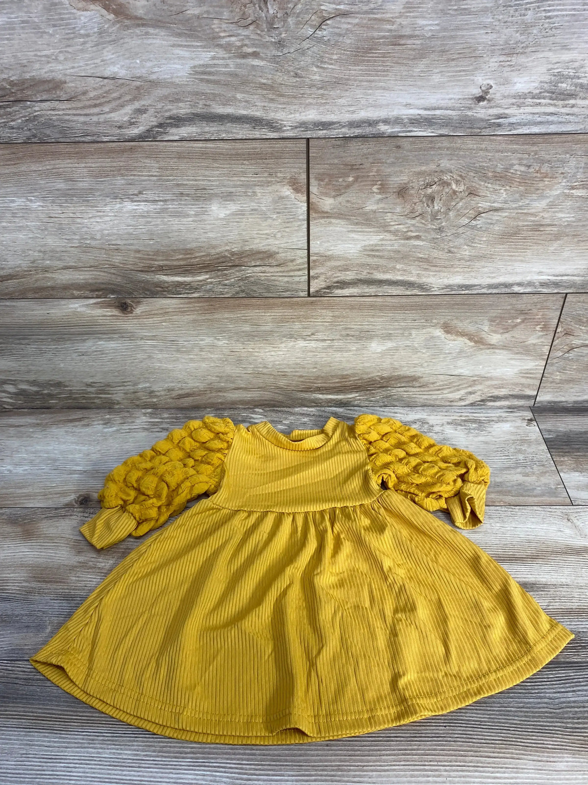 Yellow corduroy baby dress with textured long sleeves on wood background