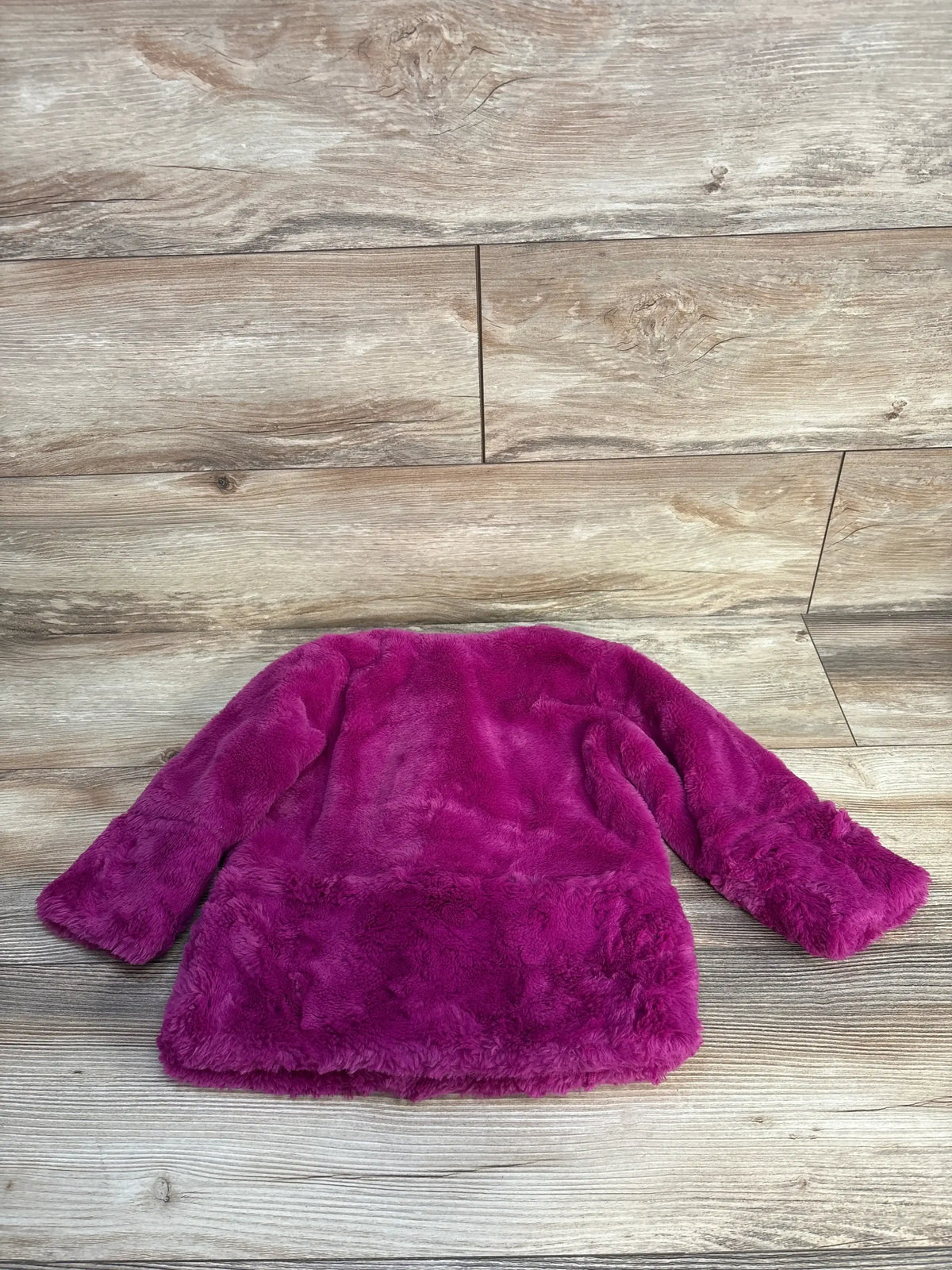 Plush magenta faux fur jacket on wooden floor background