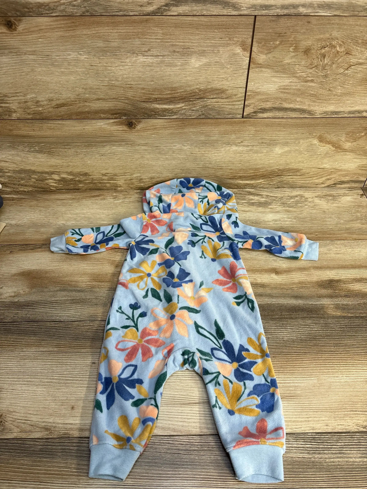 Top-down view of Carter’s hooded fleece coverall (3-6M) showcasing multicolored floral print and cuffed ankles on wooden floor