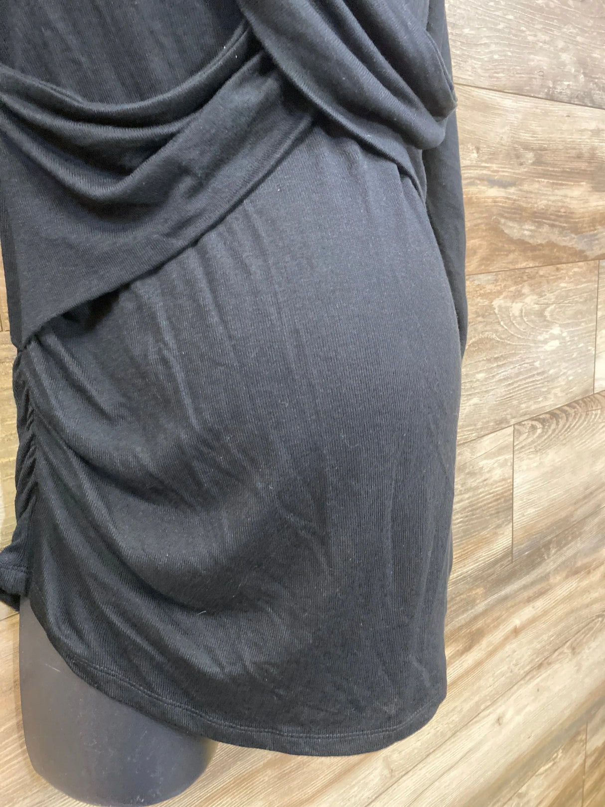 Black maternity dress on a mannequin with ruched sides, wood panel background.