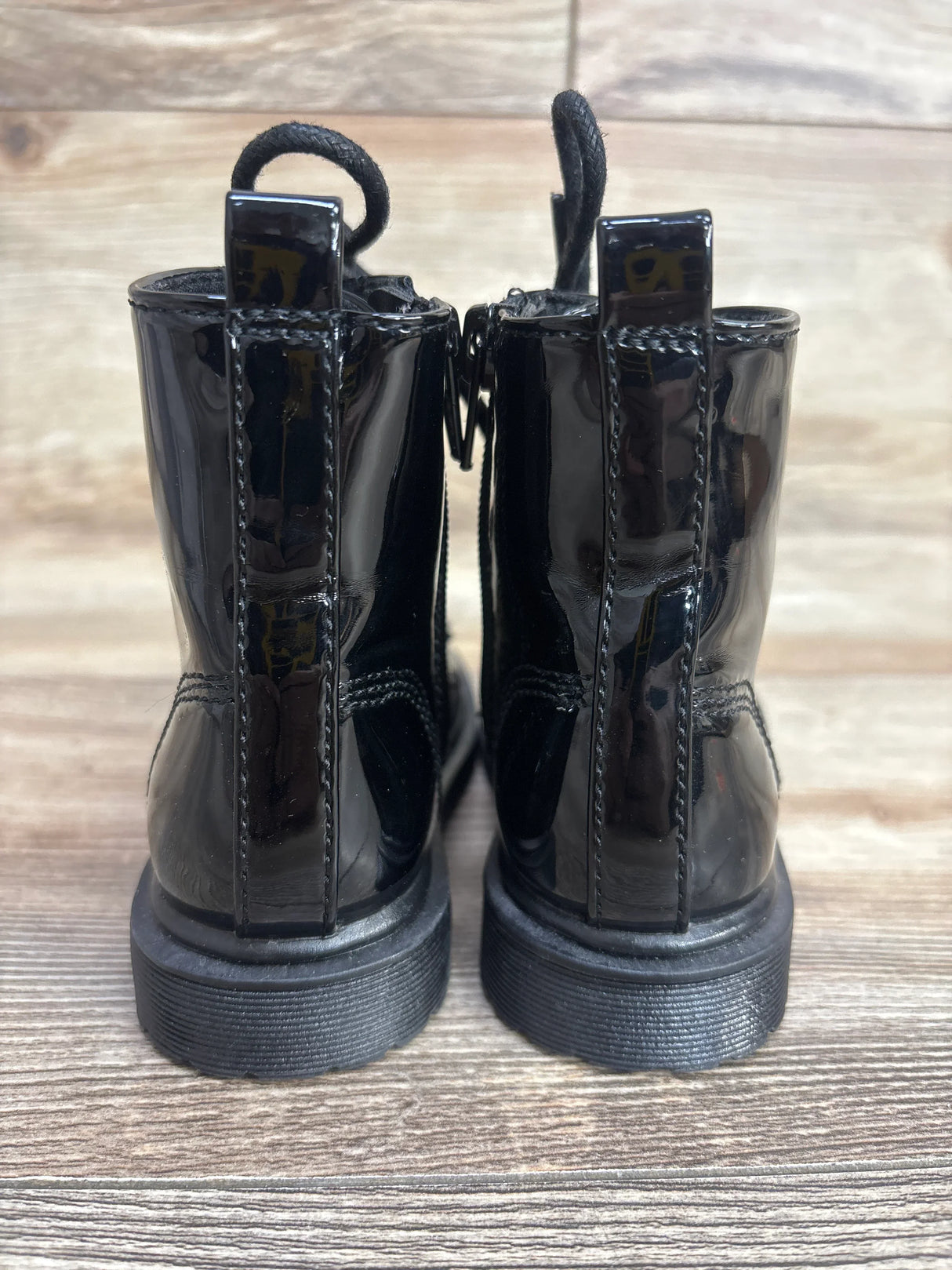 Rear view of shiny black kids lace-up boots on wooden floor