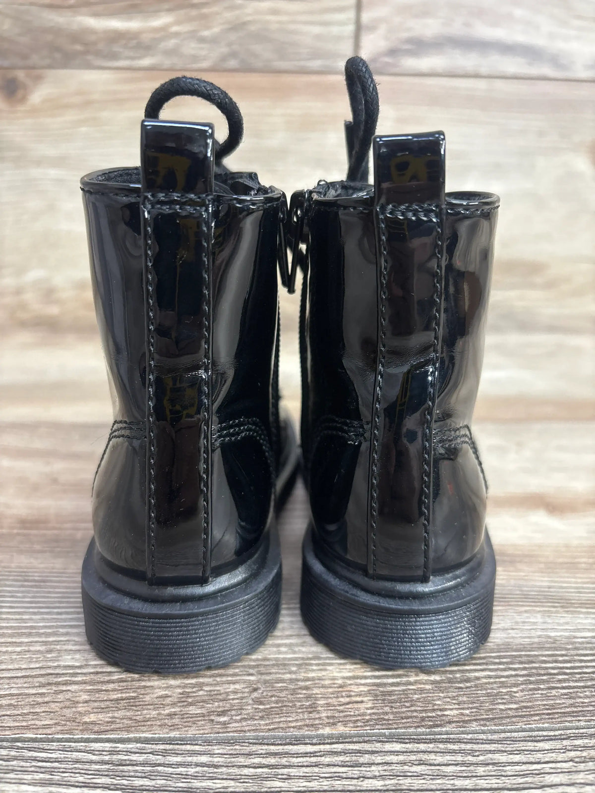 Rear view of shiny black kids lace-up boots on wooden floor