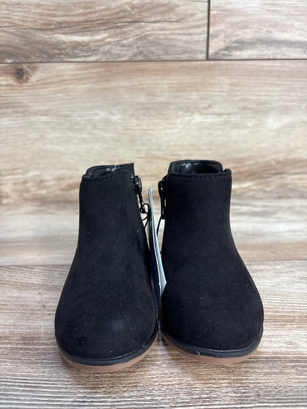 Pair of black suede ankle boots with side zippers on a wooden floor