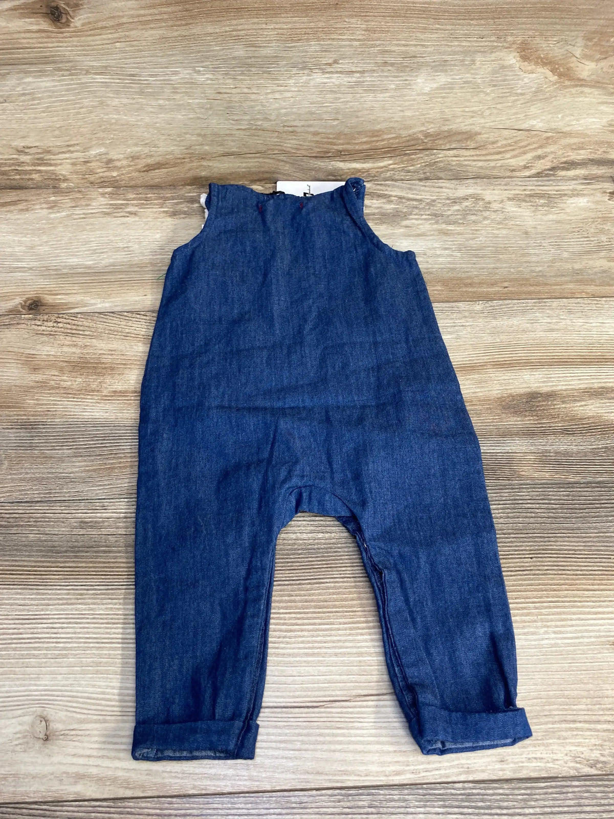 Flat lay of blue chambray baby jumpsuit size 3-6M showcasing cuffed pant legs and snap shoulder closures on wood background