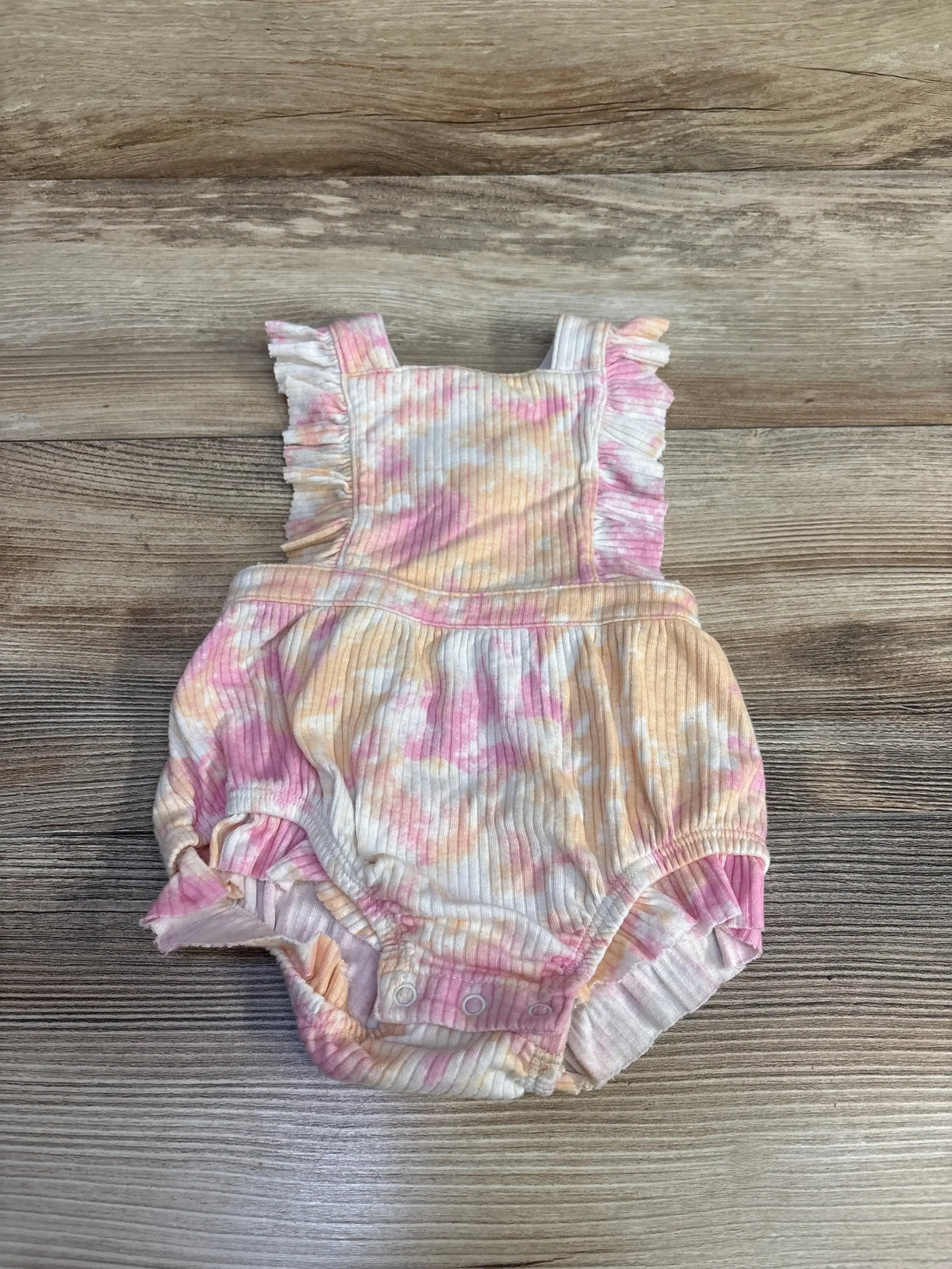 Front of Cat and Jack pink tie-dye romper with ribbed fabric, ruffle straps and snap crotch on wood background