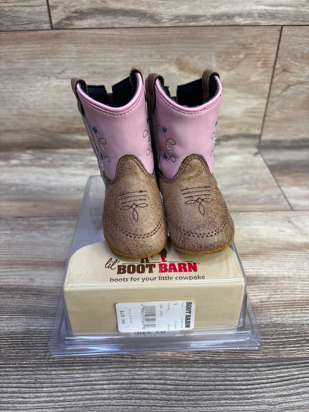 Front view of toddler cowboy boots with brown suede toes and pink embroidered shafts on clear display box over wood background