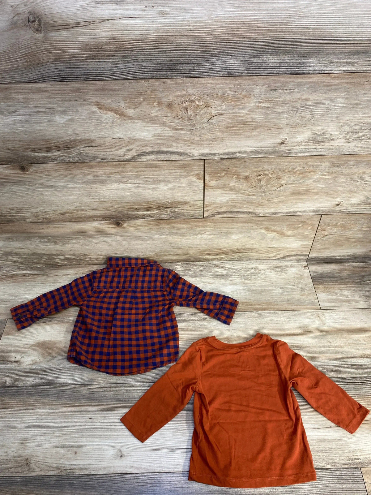 Orange and navy checkered toddler shirt and plain orange long sleeve shirt on wood floor