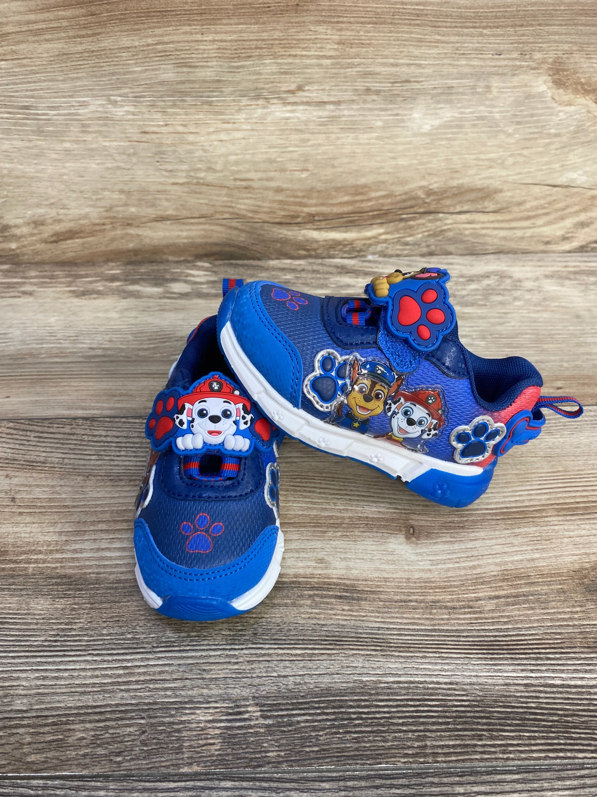 Kids' blue Paw Patrol sneakers with character decals and paw prints on wooden floor