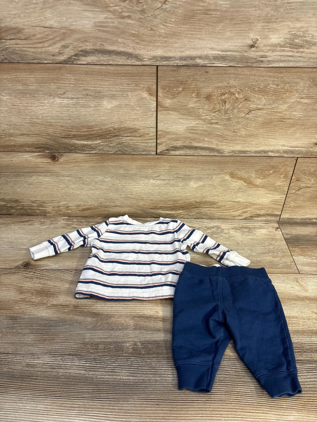 Top-down view of Just One You baby set with white striped shirt, long sleeves, and navy pants on wood-look flooring