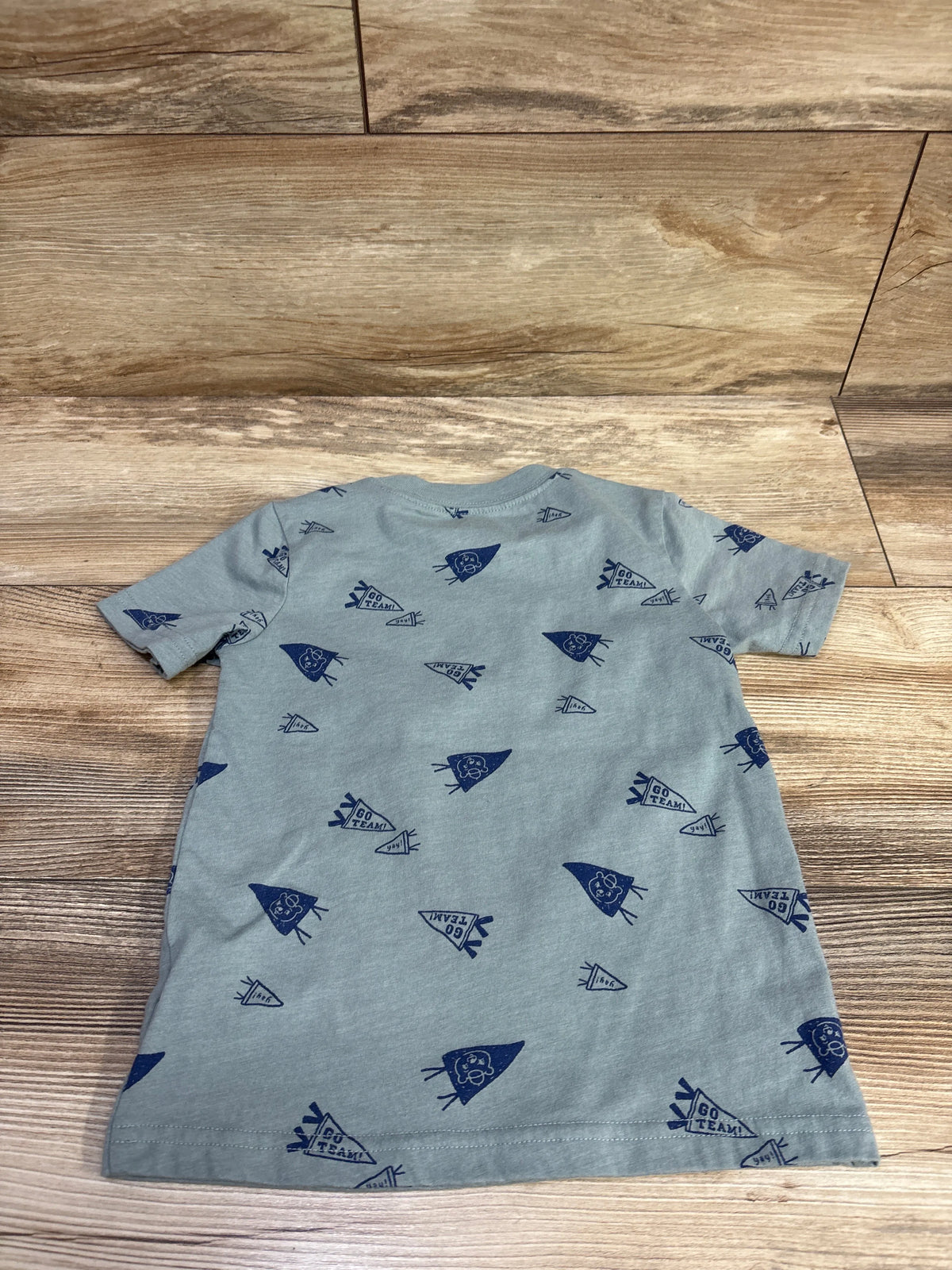 Front view of Carter’s green shirt in size 3T showcasing short sleeves and navy pennant print with a wood background