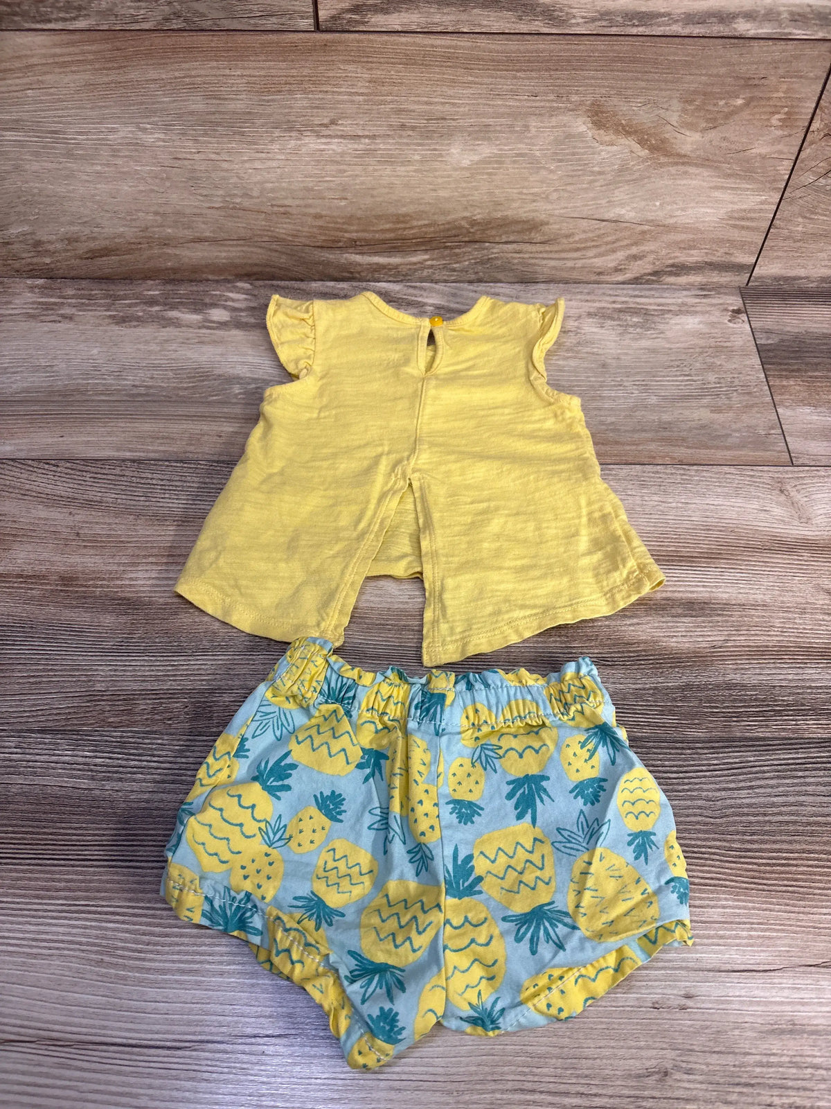 Front view of Just One You 2pc pineapple tank top and shorts set, yellow top with pineapple print shorts on wood floor