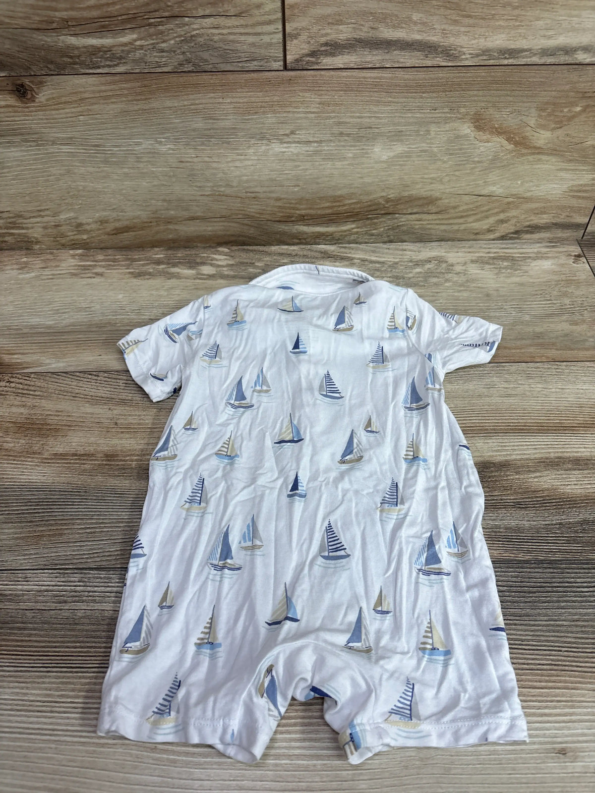 Flat lay of Angel Dear Bamboo Polo Shortie Romper in white with blue sailboat print on a wood background
